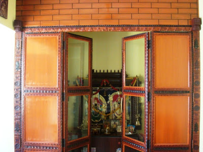 The puja room has a teak wood door with carvings and a faux brick at the top