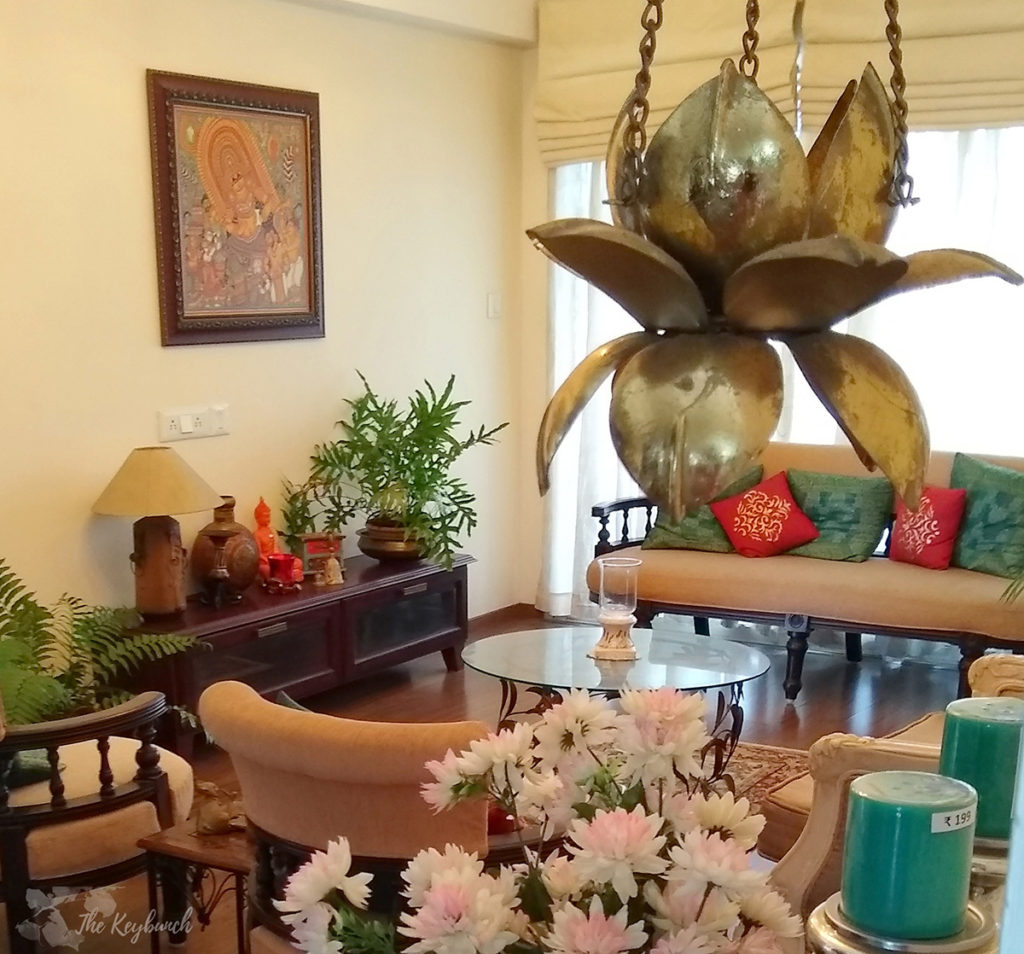 Jayashree Rajan's garden apartment tour on The Keybunch: Living room with mural painting, green plants and brass hanging diya