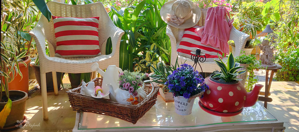 Jayashree Rajan's garden apartment tour on The Keybunch: A Candy striped cushions, red teapot, candle stand, bird cage and flower vase on green garden