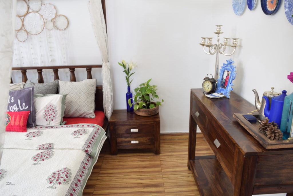 Home decor Tour by Ankita and Sitanshu’s in Lucknow - The bedroom filled with dark wood, green plants, blue frame, candlebra and assorted jugs