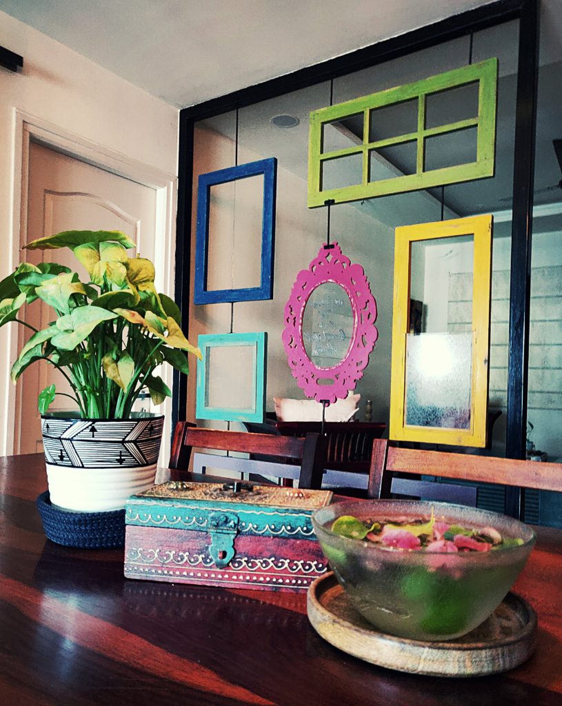 Home style Tour with Rajni in Hyderabad: the dining room is filled with beautiful colorful frames, green plants, mini trunk box and a bowl of fresh flowers