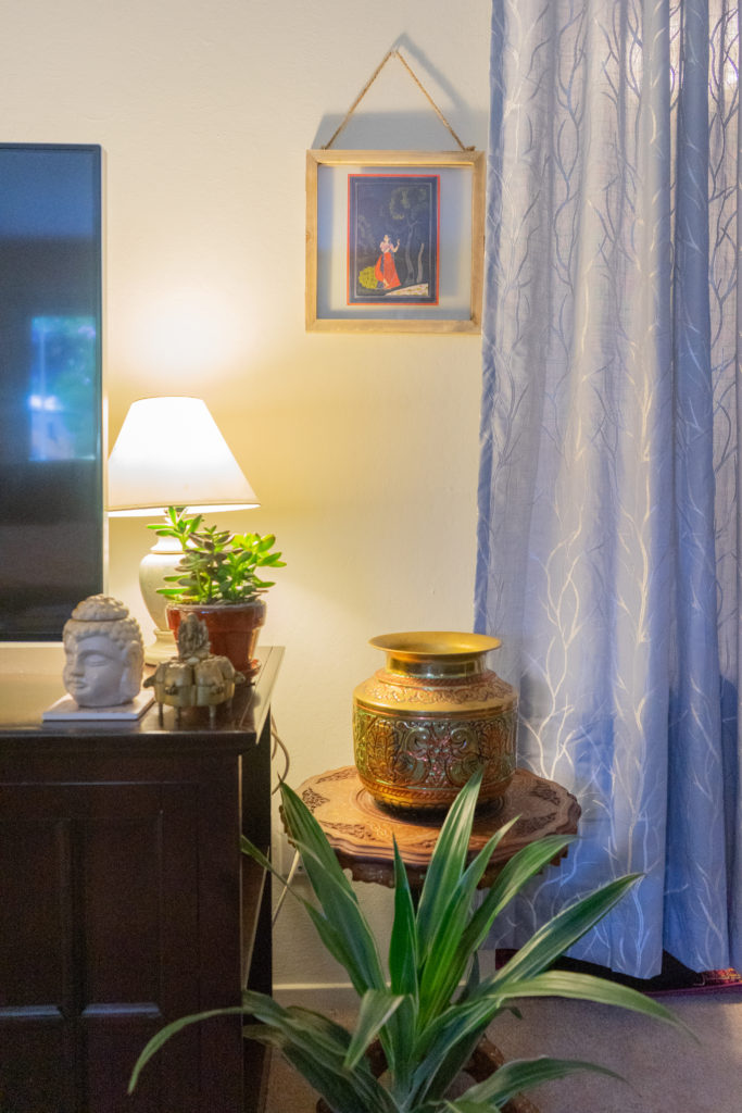 Affinity for antiques and collection of vintage | Home tour of Rushika & Dipkal's - the collection of brass pot, buddha, oil painting, lamp, and plants at the corner of the living room
