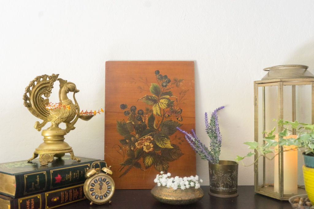 Affinity for antiques and collection of vintage | Home tour of Rushika & Dipkal's - the collection of brass bowl, brass diya, oil painting, candle stand, books and plant at the corner of the room