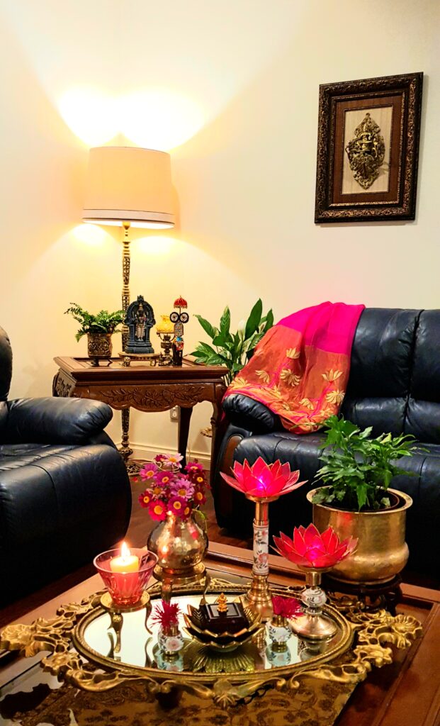 The living room is decorated with fresh flowers, glass candle stand, green plants, lotus candle stand, brass collection and vintage items