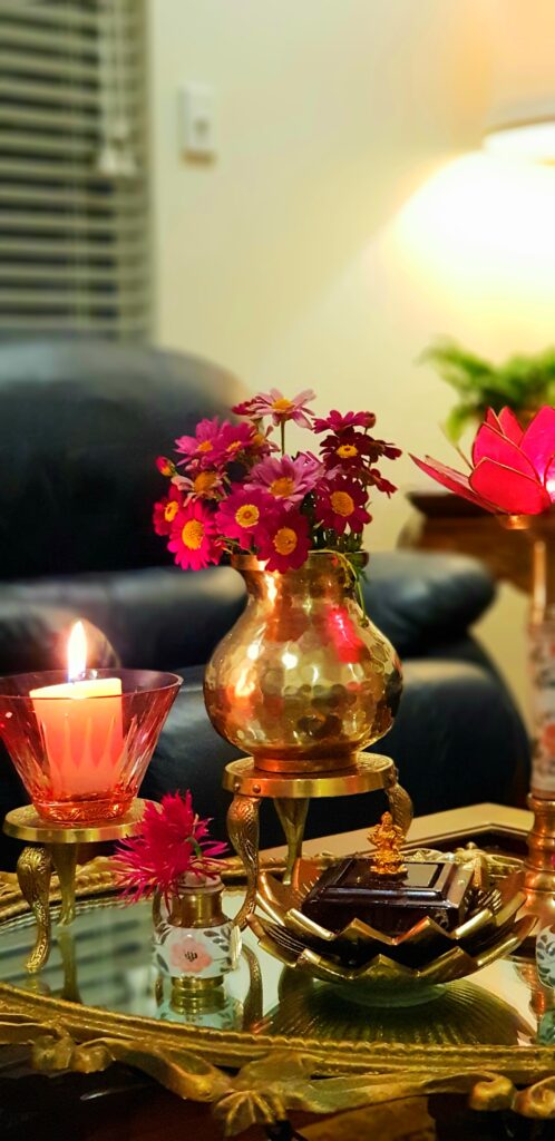 The table in the living room is setting up with fresh flowers, glass candle stand and brass collection on it