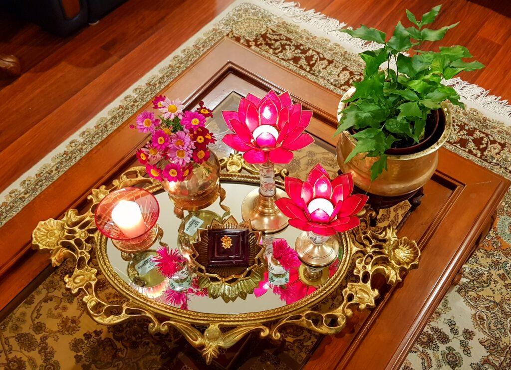 The table in the living room is setting up with fresh flowers, glass candle stand, green plants, lotus candle stand and brass collection on it