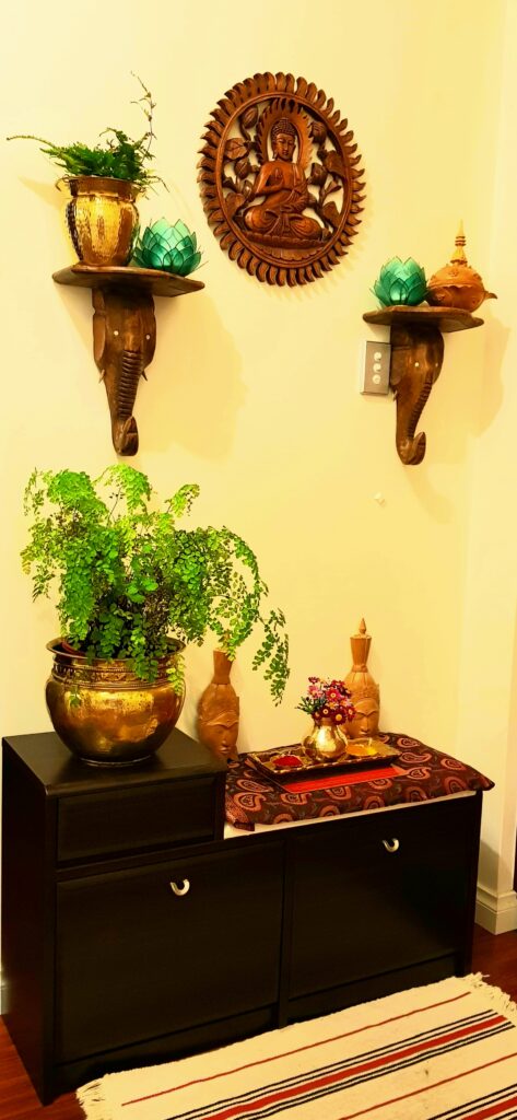 hand carved wood buddha frame, brass collection, green plant at brass vase at the corner of the room