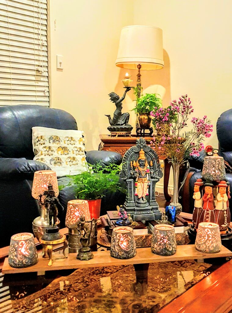 The table in the living room is decorated with diwali metal diyas, fresh flowers, sculpture and green plants