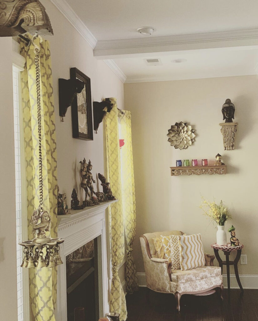 The corner of the room is decorated with vintage brass, wall frame, buddha sculpture, fresh flowers and chair