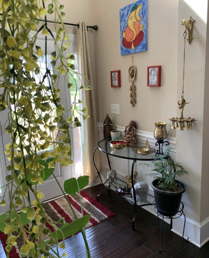 The entry way is decorated with green plants, vintage items, brass diyas and wall frames