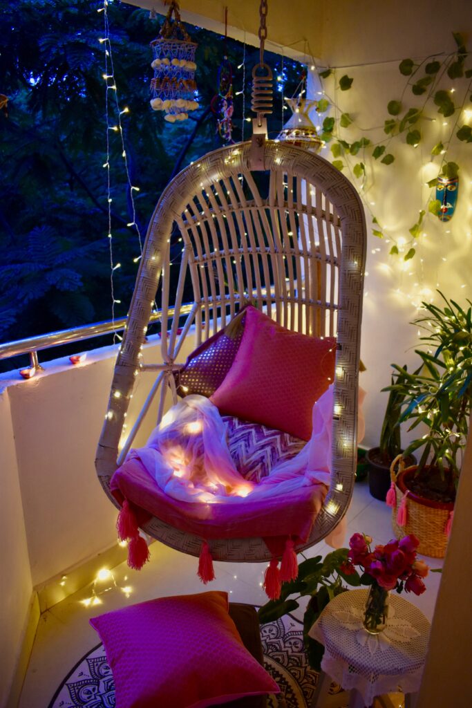 The balcony is decorated with light around the swing chair and Pom-Poms make from wool is used for the shawl swing chair cover and for the jute basket planter. 
