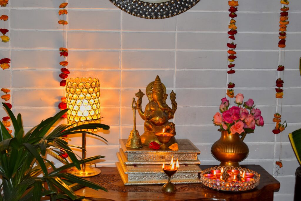 the pooja room is decorated with fresh flowers, lamp, diya, ganpati and green plants