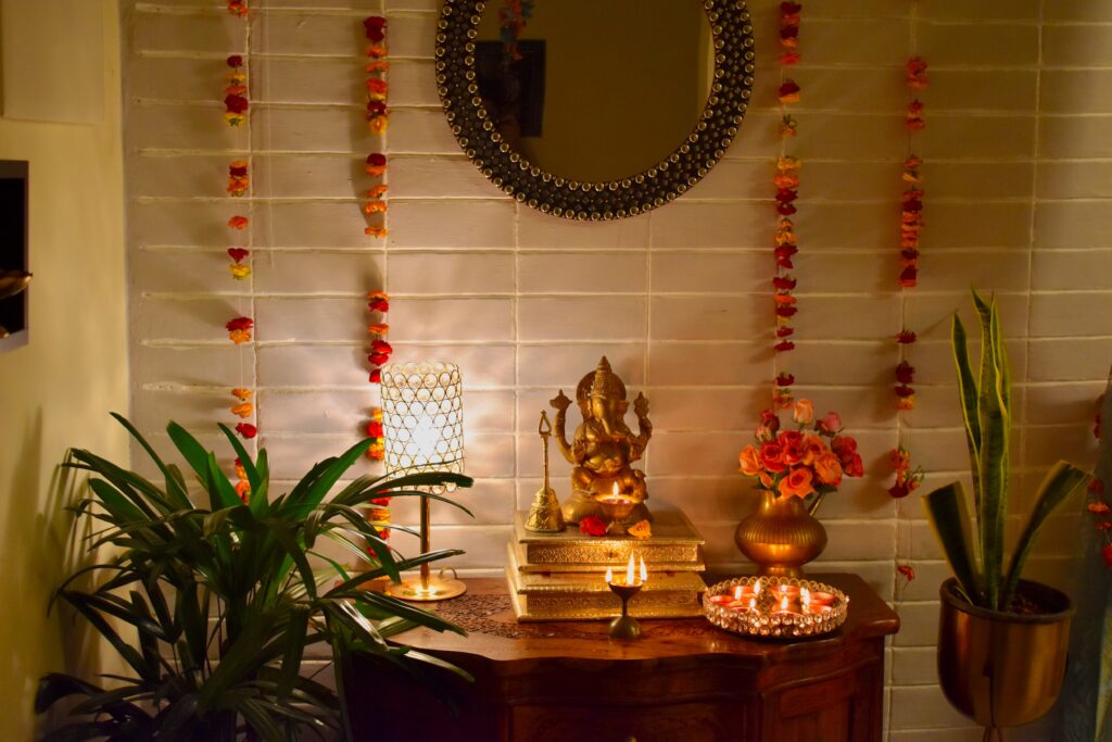 the pooja room is decorated with fresh flowers, lamp, diya, ganpati and green plants