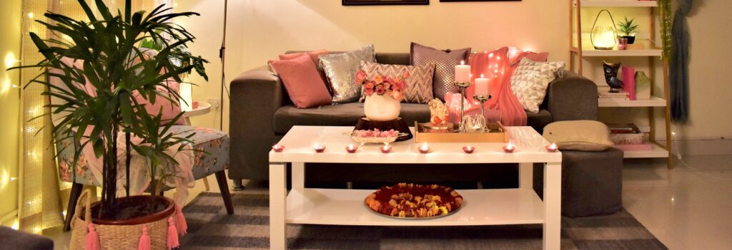 Diwali living room is decorated with pink cushion cover, diyas, and green plants