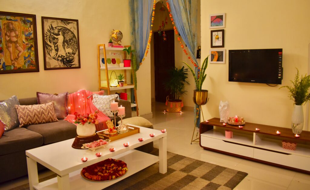 Diwali living room is decorated with pink cushion cover, diyas, wall frame and green plants