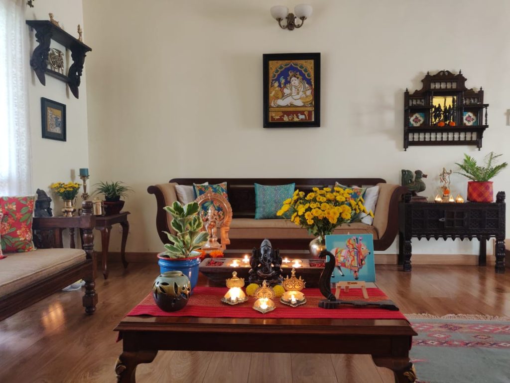The table at the living room is setting up with fresh flowers, diyas, sculpture, green plants and Pichwai frame