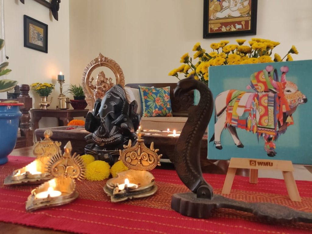 The table at the living room is setting up with fresh flowers, diyas, sculpture, green plants and Pichwai frame