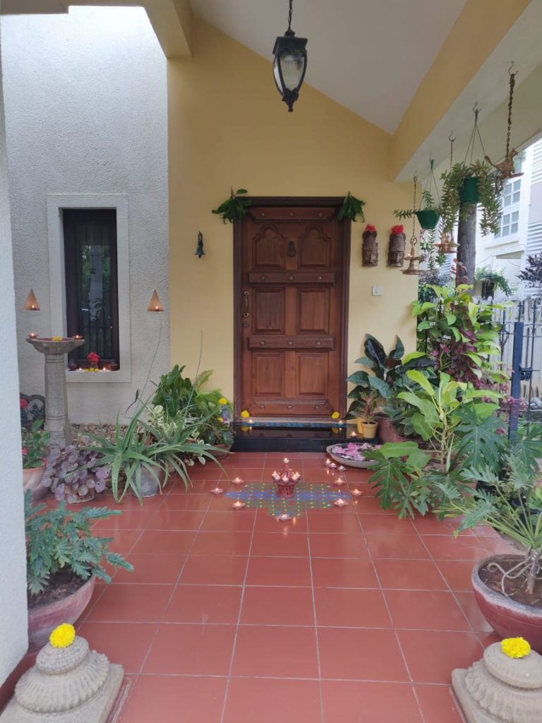 The front door entry is surrounded by green plants, and decorated with rangoli and light diyas for diwali festival