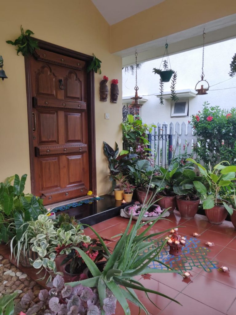 The front door entry is surrounded by green plants, and decorated with rangoli and light diyas for diwali festival