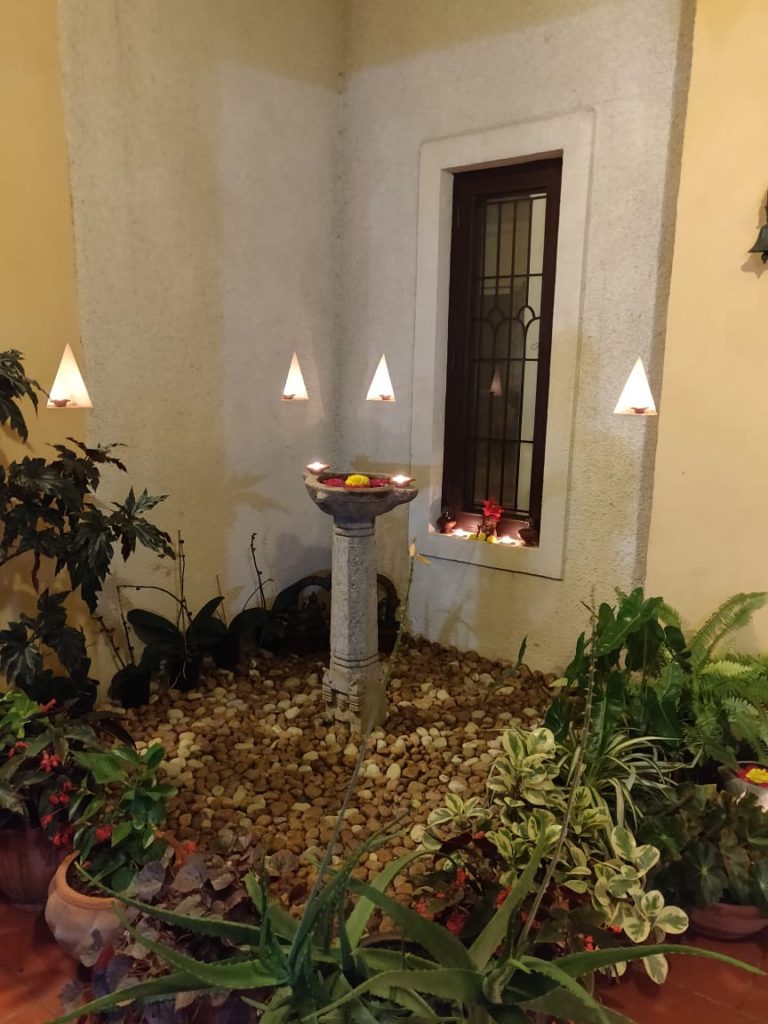 diyas, green plants and fresh flower rangoli at the corner of the front door entry