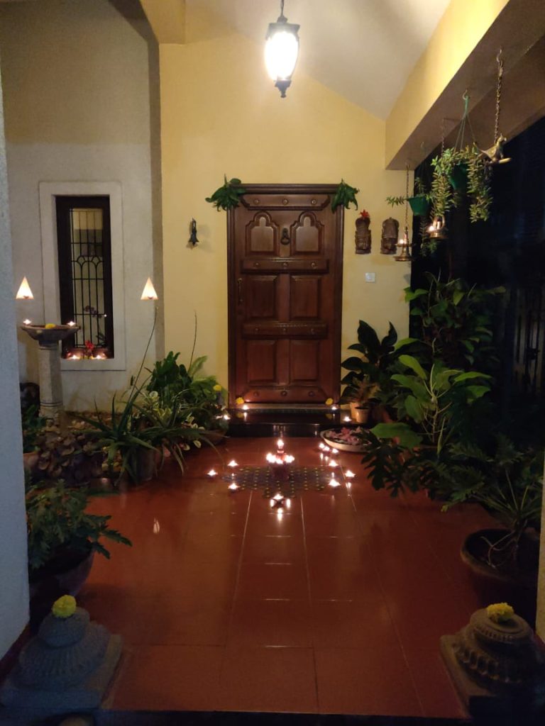 The front door entry is surrounded by green plants, and decorated with rangoli and light diyas for welcoming the diwali festival