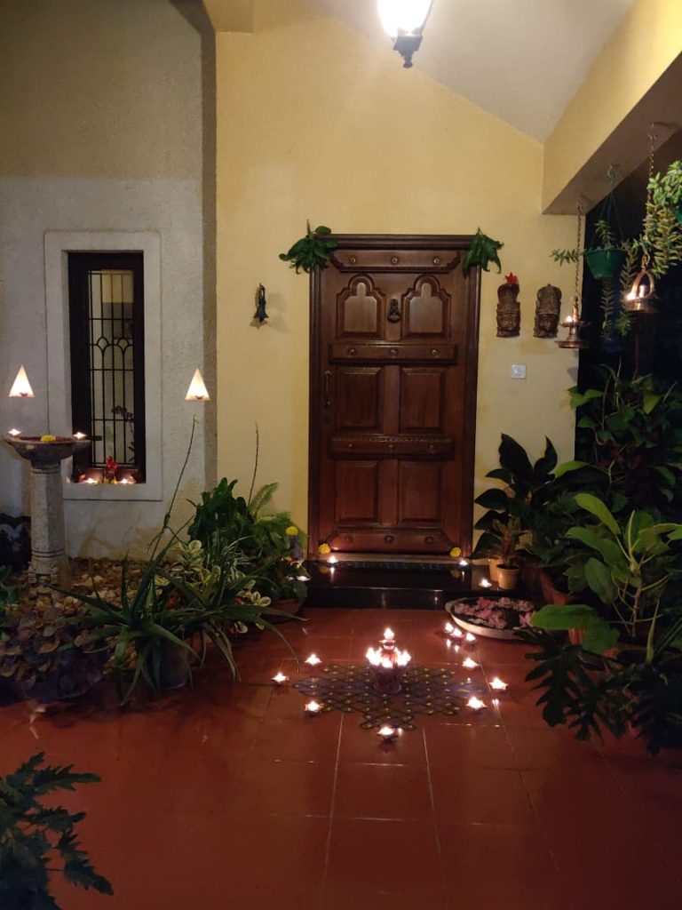 The front door entry is surrounded by green plants, and decorated with rangoli and light diyas for welcoming the diwali festival