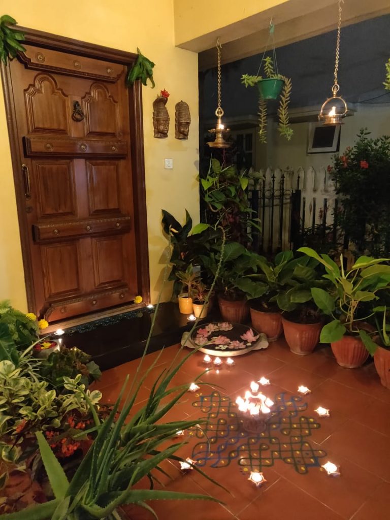 The front door entry is surrounded by green plants, and decorated with rangoli and light diyas for welcoming the diwali festival