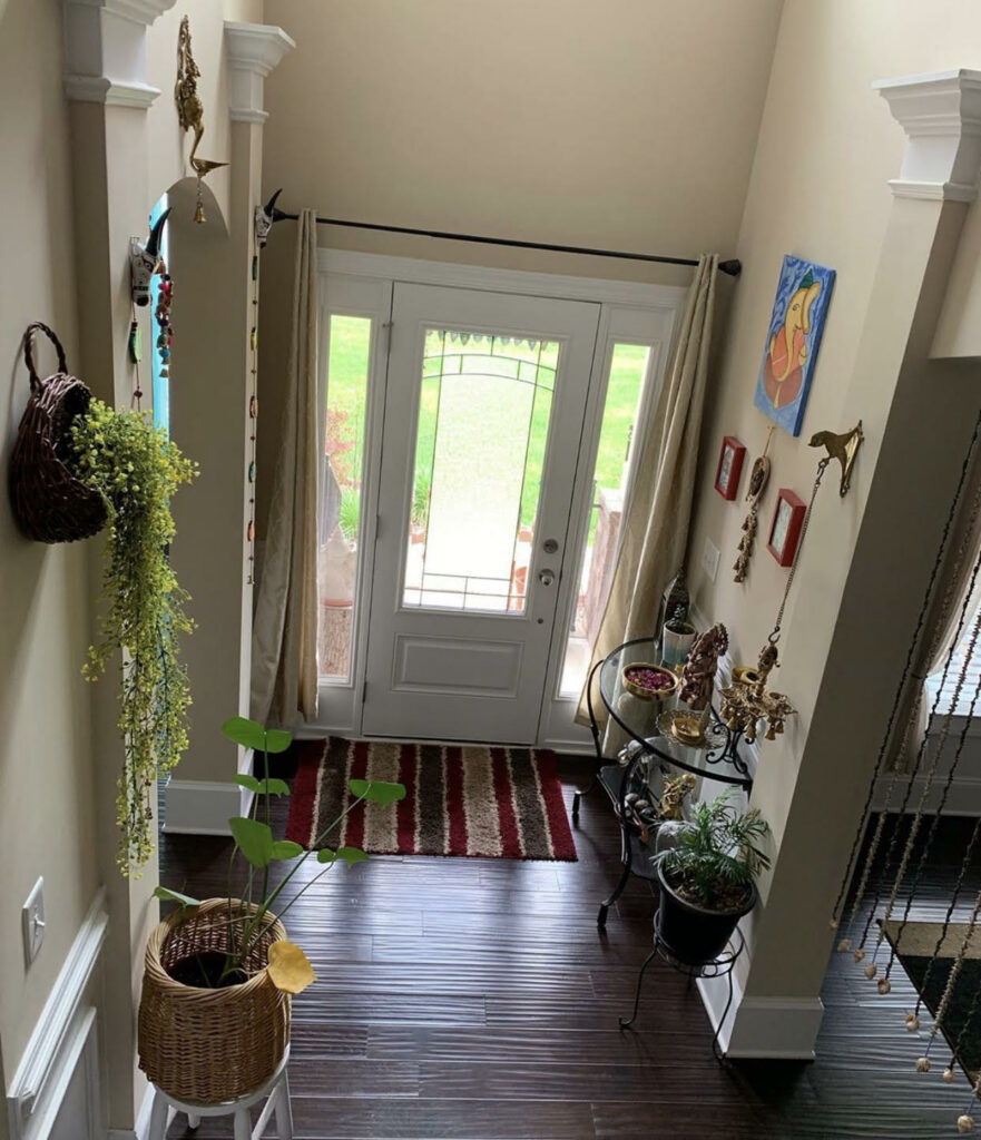 The entry way is decorated with green plants, vintage items, brass diyas and wall frames