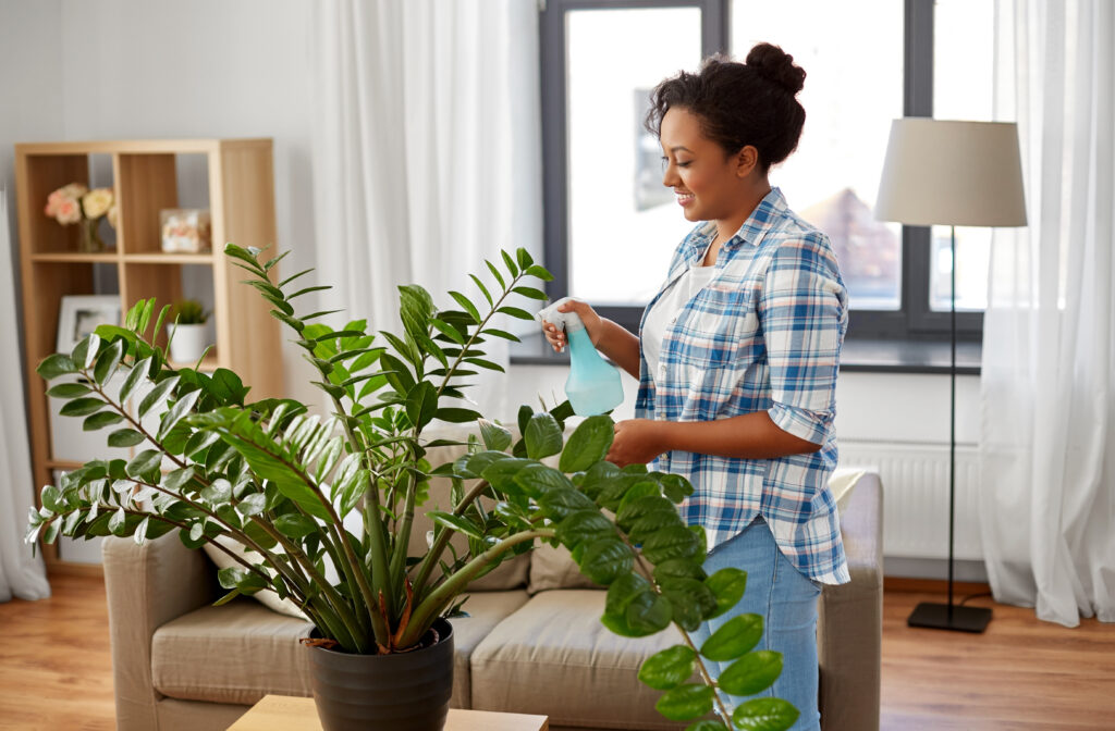 happy woman spraying houseplant with water sprayer at home.