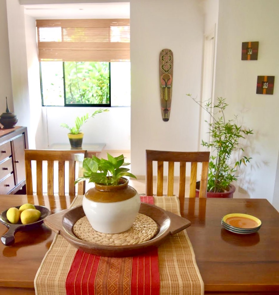 The dining space is decorated with green plants, wooden mask, and beautiful center piece on dining table | ASHA RAJ home tour
