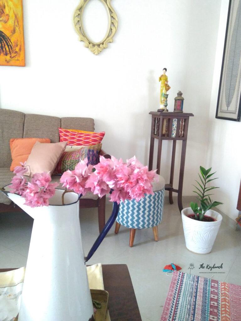 The living room is styling up with colorful cushion cover, zz green plant, bougainvillea flower, ottoman chair and vintage side table | Areas where an Interior Stylist can help you | Thekeybunch decor blog