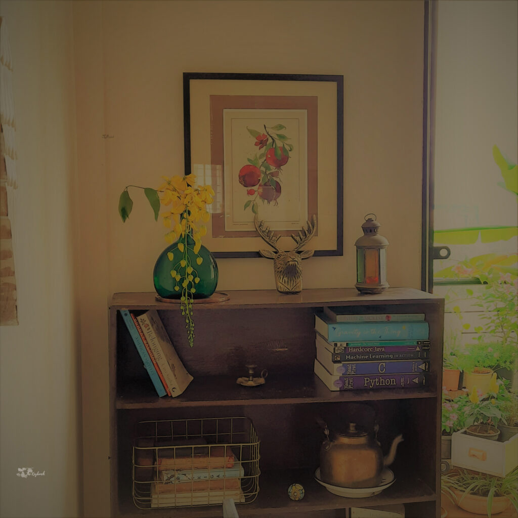 Decorate with a touch of yellow during the pandemic | Yellow flowers, frame, animal skull, collection of books, brass candle stand, kettle brass at wooden shelves at the corner of the living room