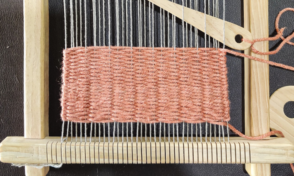 A closeup of a home loom, with orange eri silk thread forming an unfinished tapestry | 6 Tapestry DIYs on Muezart's home-use loom