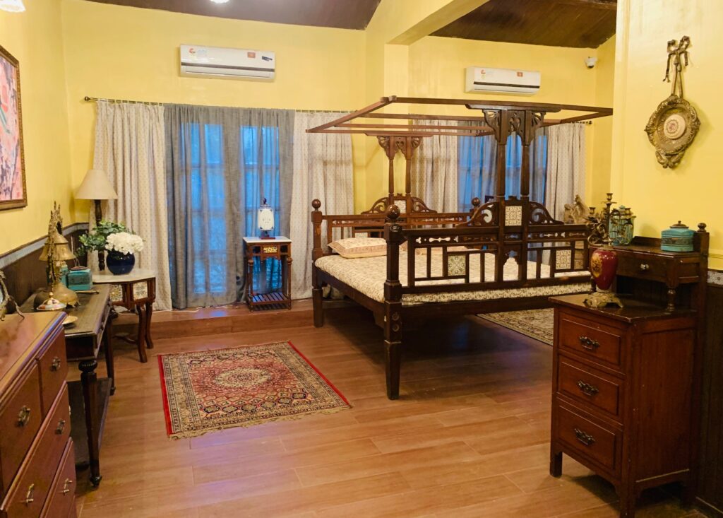 Villa Rashmi - A Heritage Gem in Mumbai | Traditional Indian bed with lamp on side table, wall frames, wooden table and vintages decorated at the bedroom | TheKeybunch decor blog