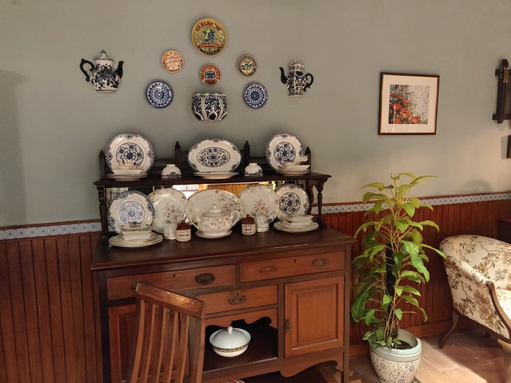 Villa Rashmi - A Heritage Gem in Mumbai | The living room wall was decorated with wall plate and wall mounted kettle, and the ceramic plates on top of wooden cabinet | TheKeybunch decor blog
