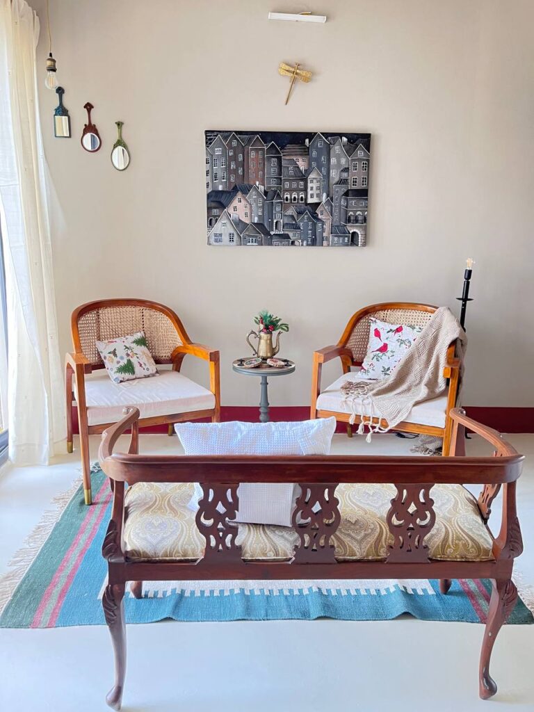 living room with 2 statement chairs by the rose and teak, and an antique bench. a cityscape adorns the wall by artist christine kale