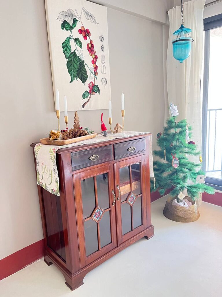 a painting of a coffee plant by artist christine kale, hangs above a charming sideboard decorated for christmas.